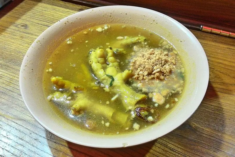 Semangkuk soto ceker berkuah kuning dengan ceker ayam utuh dan taburan koya