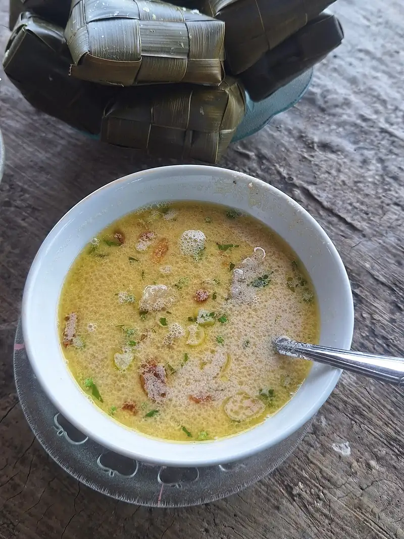 Semangkuk coto Makassar berkuah kuning keruh disajikan bersama tumpukan ketupat anyaman daun