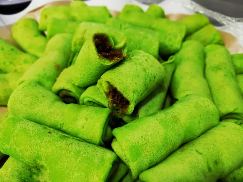 Potongan dadar gulung hijau pandan dengan isian kelapa parut bergula merah berwarna cokelat