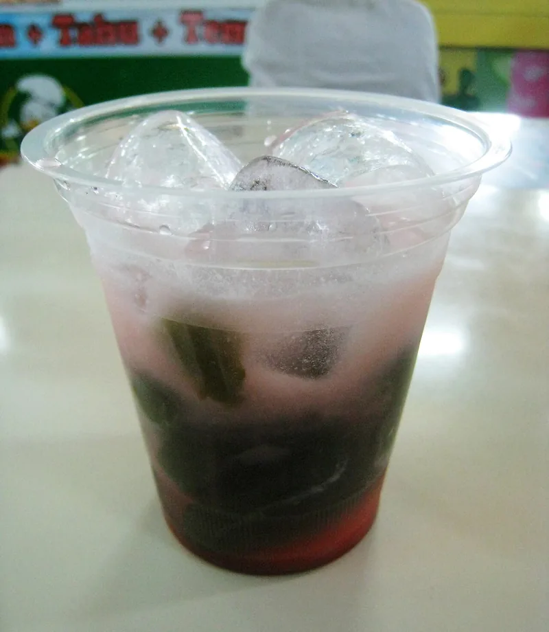 Gelas es cincau dengan potongan gel, kuah pucat, dan es batu