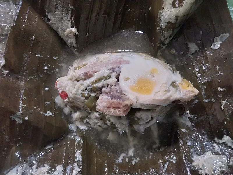 Bungkusan daun pisang terbuka berisi garang asem ayam dengan telur dan kuah santan