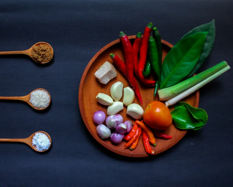 Bumbu garang asem di piring kayu: cabai merah, cabai hijau, bawang merah, bawang putih, tomat, serai, dan daun salam