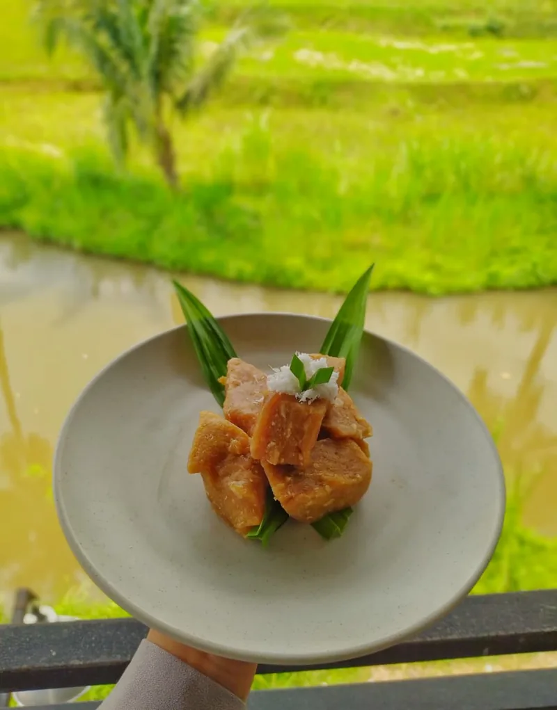 Potongan getuk singkong coklat gula merah di piring dengan daun pandan dan kelapa parut