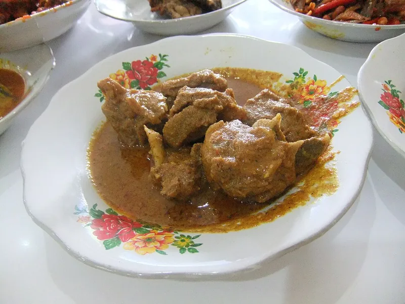 Gulai kambing masakan Padang dengan kuah kental kecokelatan di piring bermotif bunga