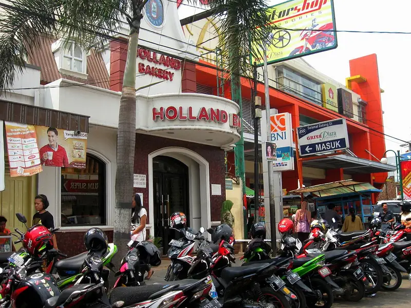 Gerai Holland Bakery Sumedang dengan poster promosi di dinding dan deretan motor parkir
