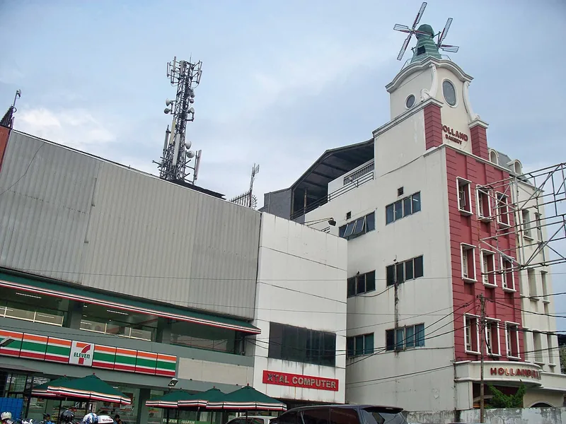 Gedung Holland Bakery bermenara kincir angin bersebelahan dengan gerai minimarket di tepi jalan