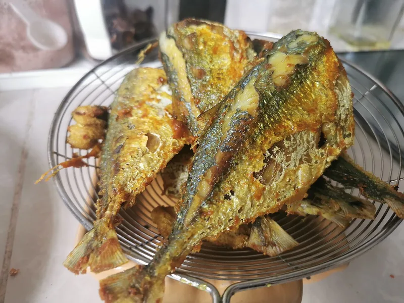 Ikan goreng kunyit berwarna kuning keemasan yang ditiriskan di atas saringan