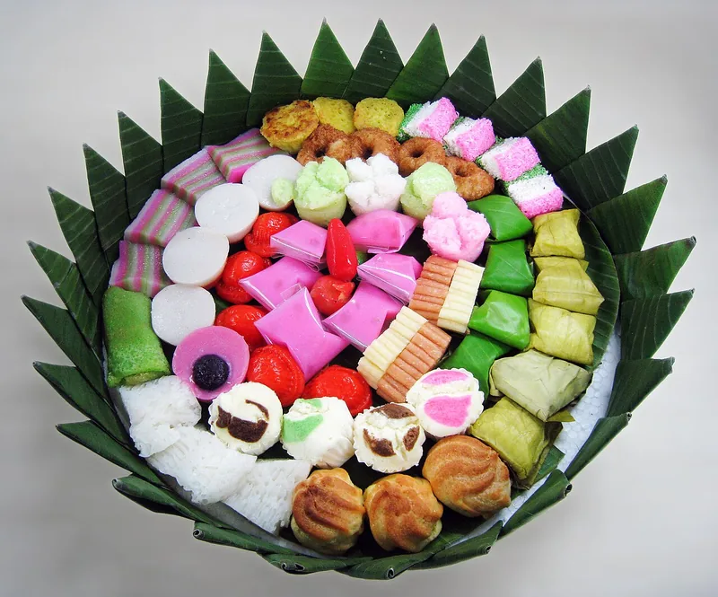 Tampah daun pisang berisi aneka kue basah warna-warni seperti kue lapis, nagasari, dan kue mangkok