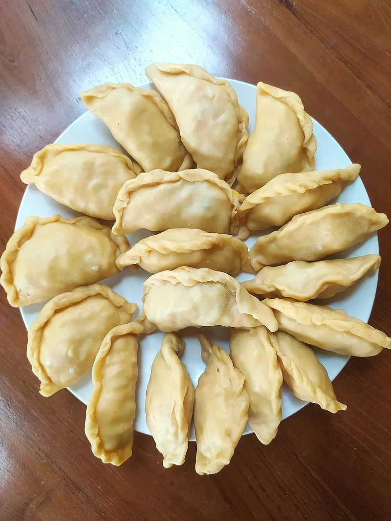 Kue pastel mentah yang sudah diisi dan dilipat setengah lingkaran dengan tepi dipilin, siap digoreng