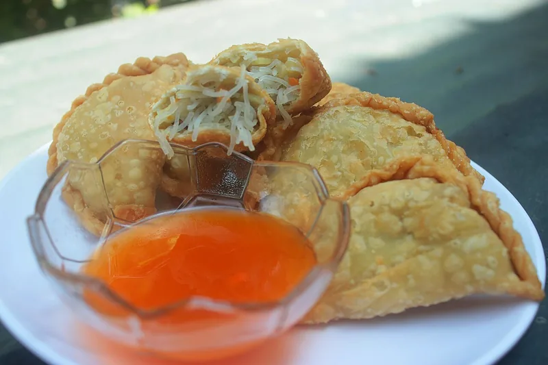 Jalangkote goreng dengan isian soun terlihat, disajikan bersama semangkuk kecil sambal cair oranye