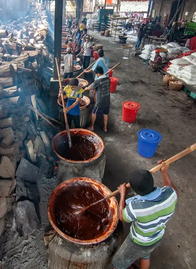 Pekerja mengaduk adonan dodol cokelat kental di kuali tembaga besar dengan dayung kayu panjang