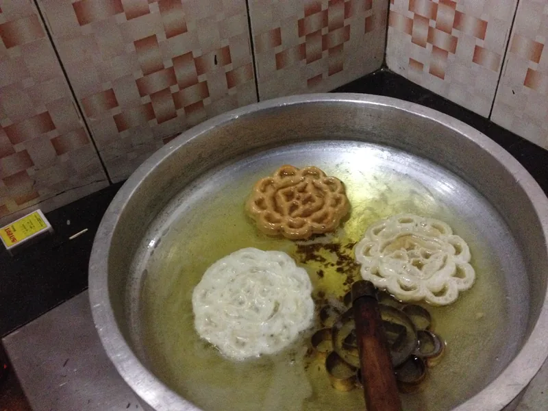 Cetakan besi berbentuk bunga dan kue goreng mengapung di minyak panas dalam wajan