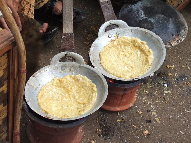 Dua wajan kecil berisi adonan kerak telor dari ketan dan telur dimasak di atas anglo tanah liat