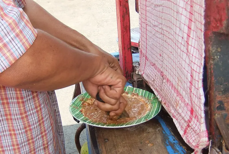 Penjual ketoprak gerobak di Jakarta mengulek bumbu kacang langsung di atas piring