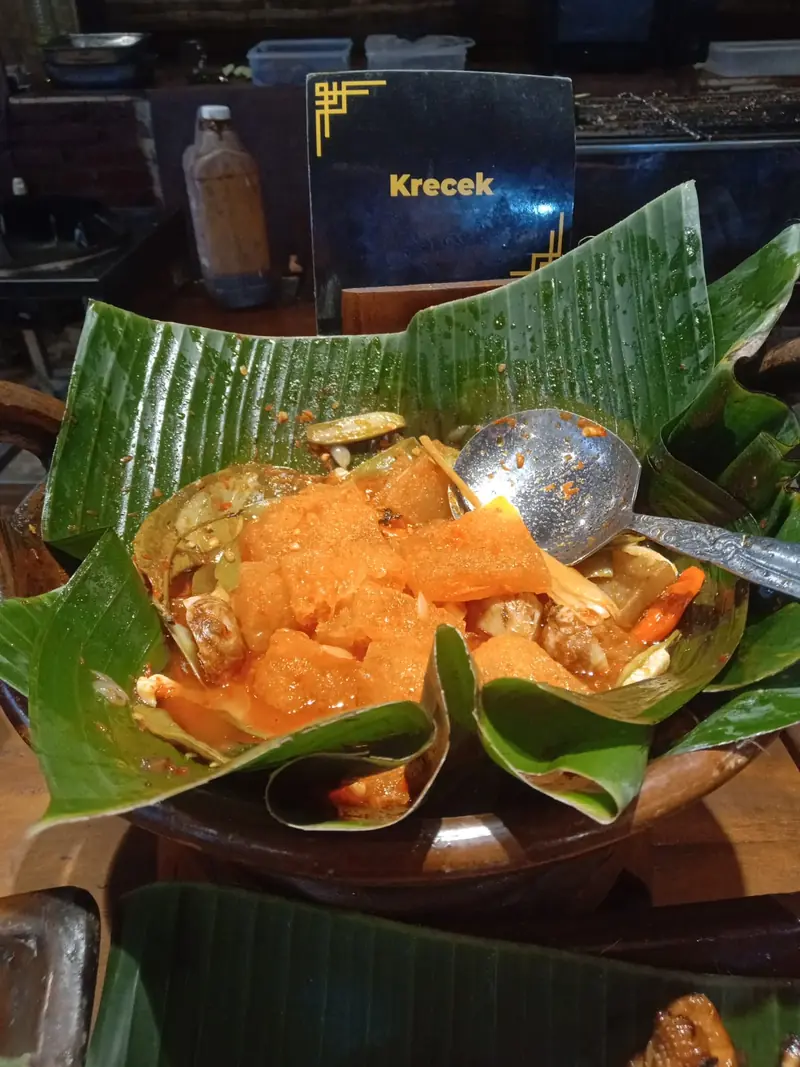 Sambal goreng krecek berkuah santan oranye dengan kerupuk kulit kenyal dalam wadah beralas daun pisang