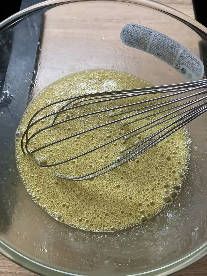 Telur dan gula dikocok dengan whisk kawat di mangkuk kaca hingga berbuih kekuningan