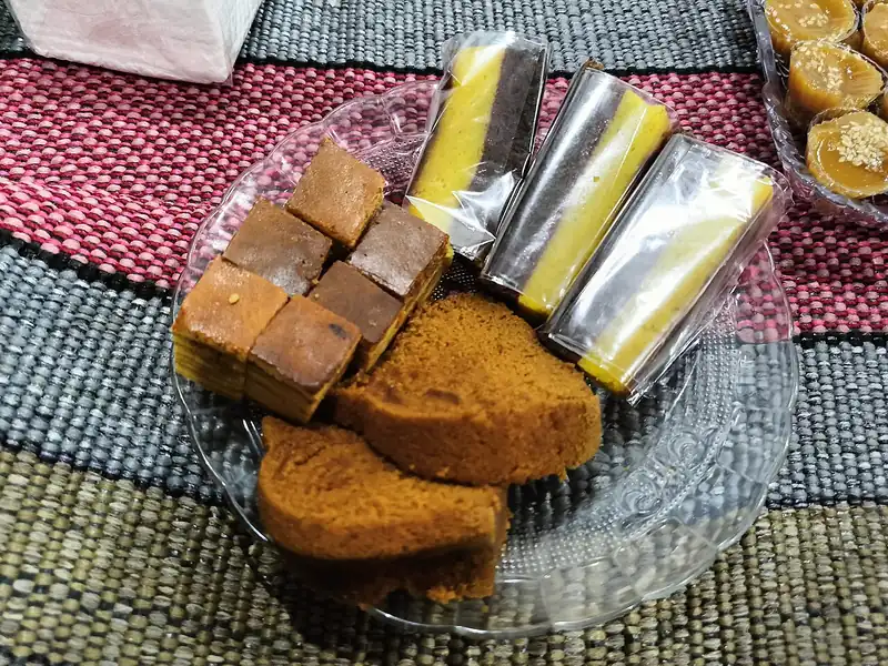 Potongan bolu cokelat, lapis legit, dan bolu gulung kemasan di atas piring kaca