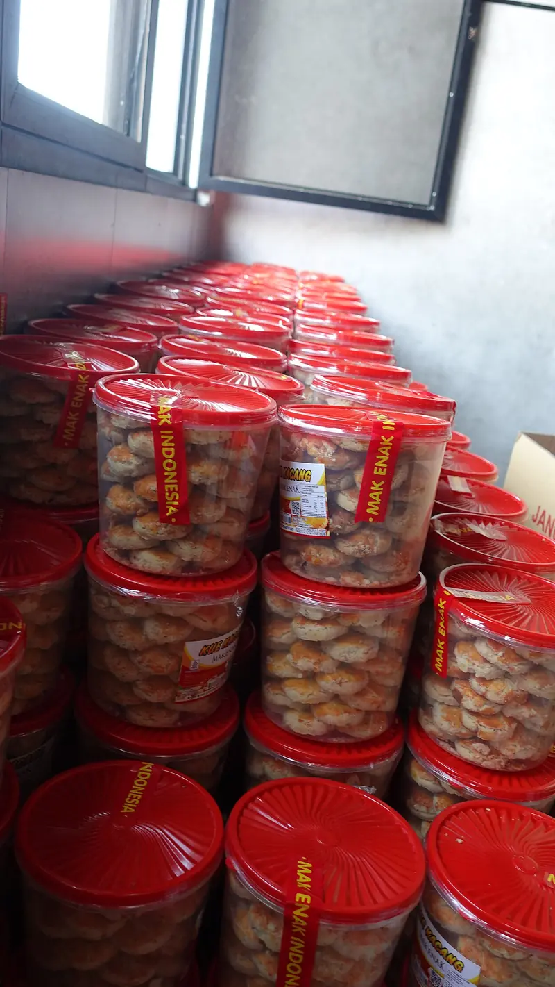 Tumpukan toples tutup merah berisi kue kacang siap jual di ruang produksi
