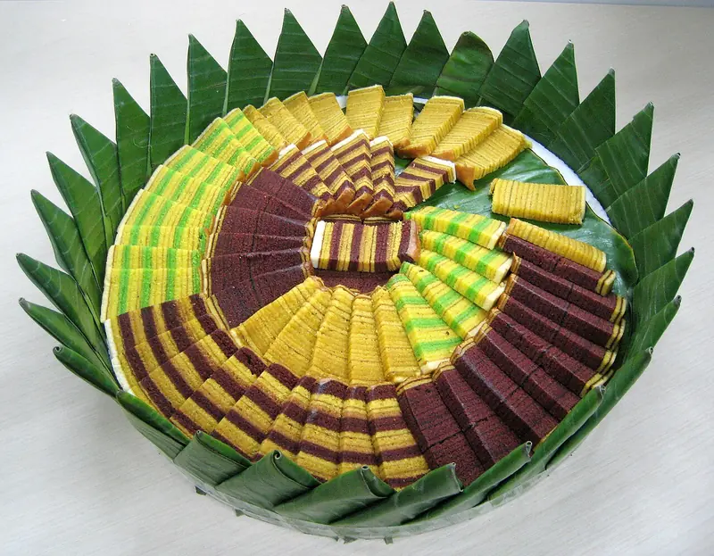Tampah beralas daun pisang berisi irisan lapis legit rasa original, cokelat, dan pandan