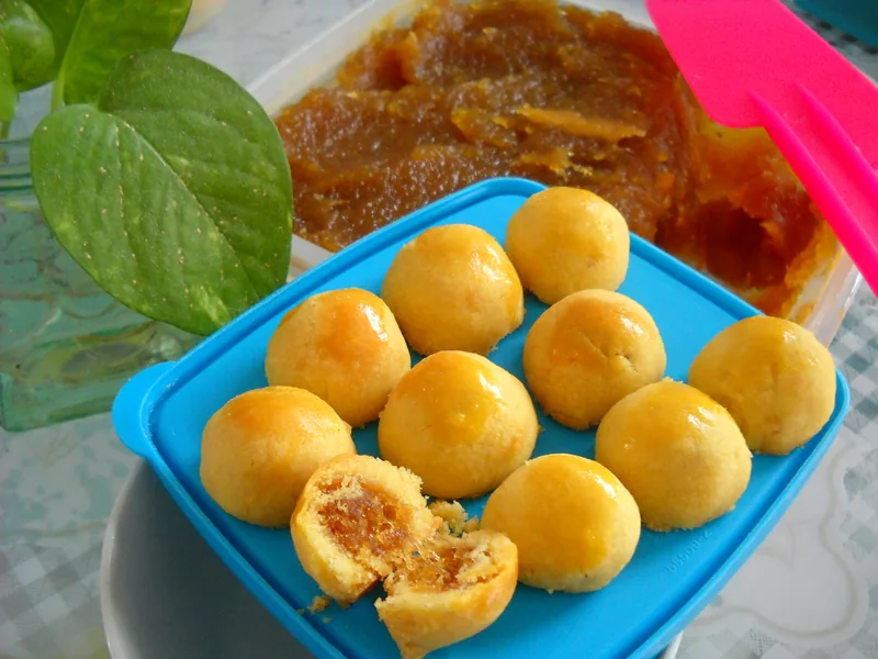 Kue nastar bulat keemasan di wadah biru, satu dibelah memperlihatkan isian selai nanas