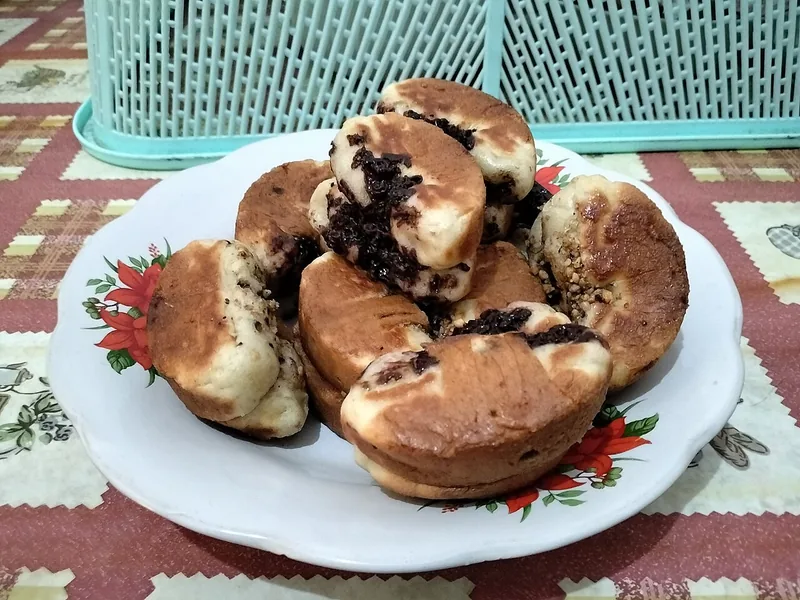 Sepiring kue pukis cokelat dengan taburan meses di atas piring bermotif bunga