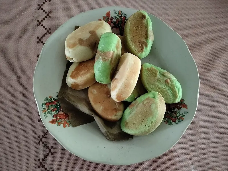 Kue pukis warna-warni hijau pandan dan cokelat di atas piring beralas daun pisang