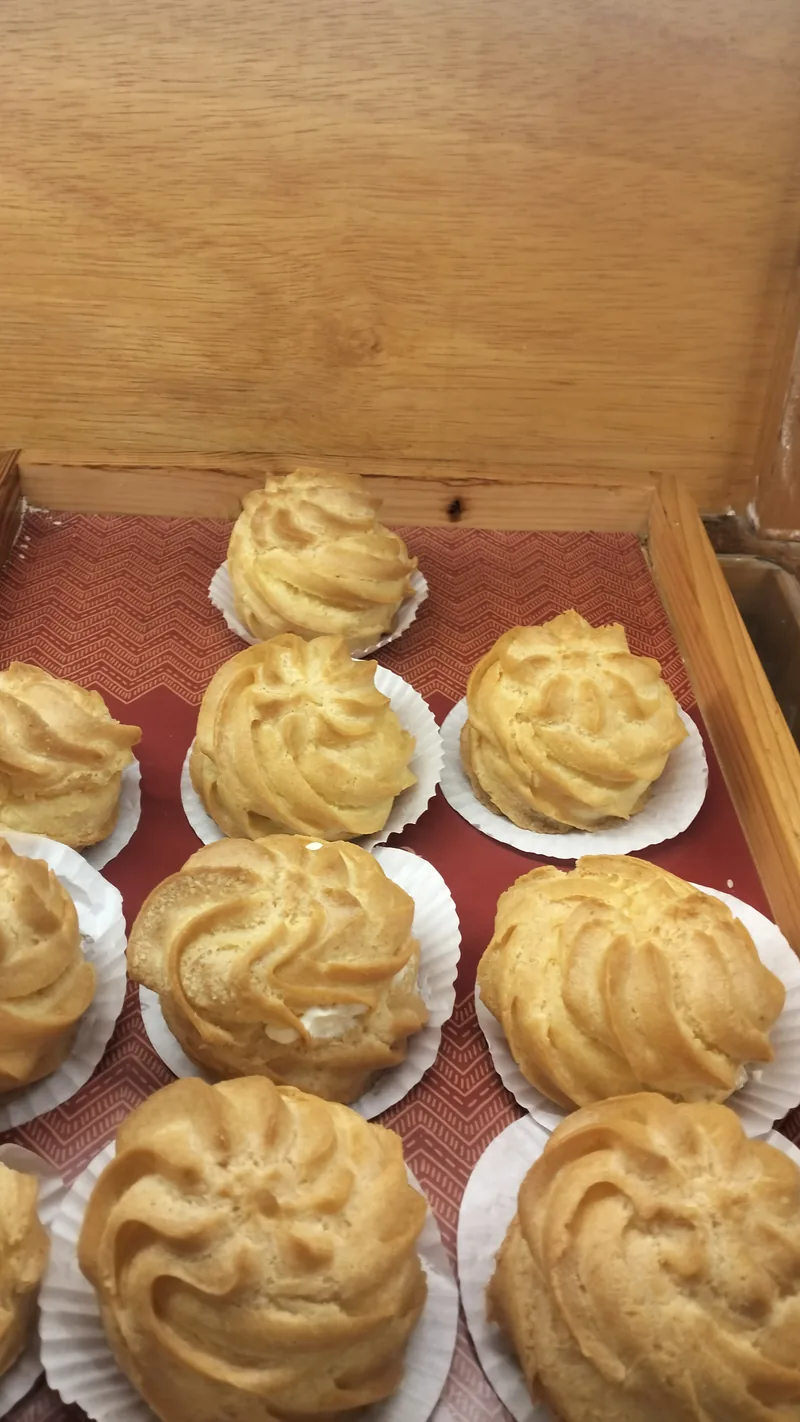 Deretan kue sus berbentuk ulir hasil semprotan spuit bintang di atas cup kertas dalam kotak kayu