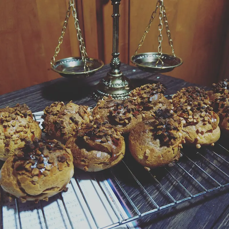 Kue sus buatan rumah bertabur cokelat dan kacang cincang di atas rak kawat pendingin