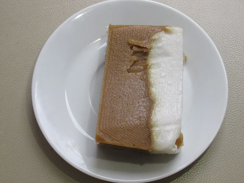 Sepotong kue talam dua lapis cokelat dan putih yang menyatu rapi di piring putih