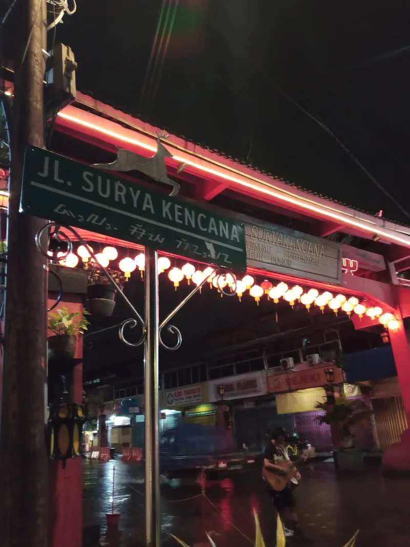 Papan nama Jalan Surya Kencana dan gapura merah berhias lampion di kawasan pecinan Bogor pada malam hari
