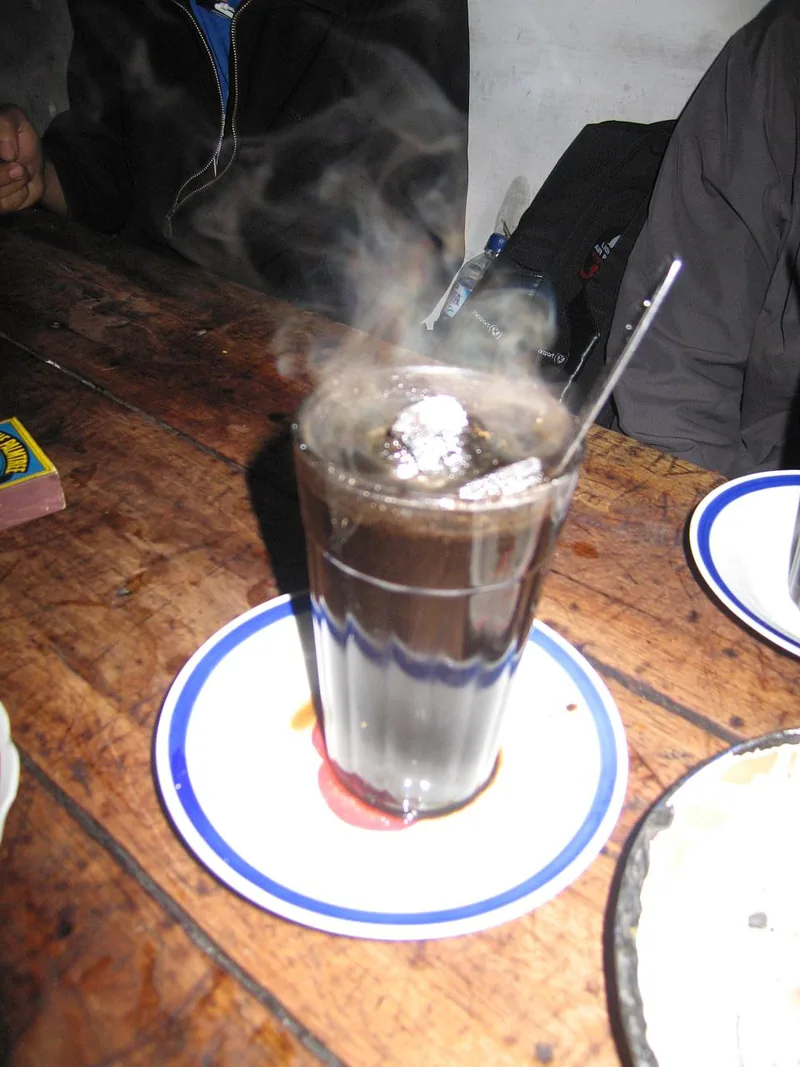 Segelas kopi joss berasap dengan arang membara di dalamnya di meja kayu angkringan