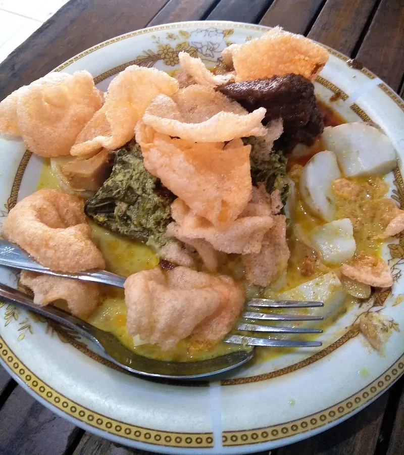 Lontong sayur Padang dengan sayur pakis, rendang, dan kerupuk merah dalam kuah gulai kuning