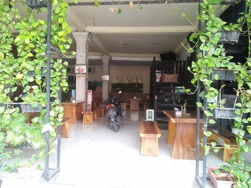 Ruang makan warung dengan meja dan bangku kayu jati serta tanaman rambat hijau di pintu masuk