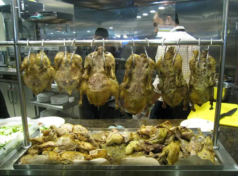Ayam betutu dan bebek betutu utuh digantung di etalase kaca rumah makan dengan potongan berbumbu di bawahnya