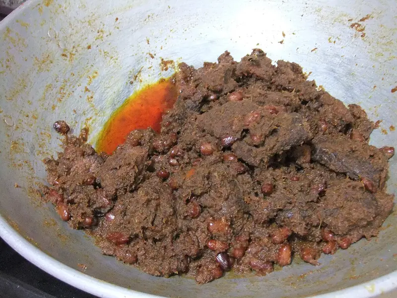 Rendang daging sapi berwarna cokelat gelap bercampur kacang merah di dalam wajan masak
