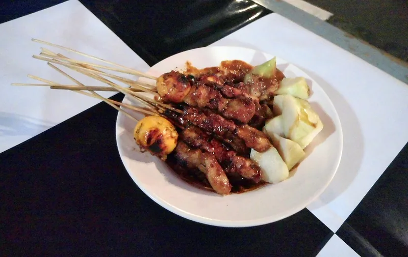Sepiring sate ayam berbumbu kecap dan kacang disajikan bersama potongan lontong
