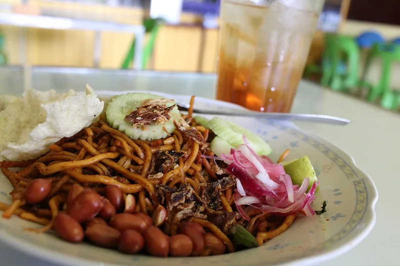 Sepiring mie Aceh goreng dengan kacang tanah, emping, irisan mentimun, dan acar bawang merah