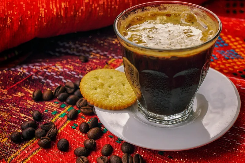 Segelas kopi hitam arabika Gayo dengan biskuit dan biji kopi di atas kain merah
