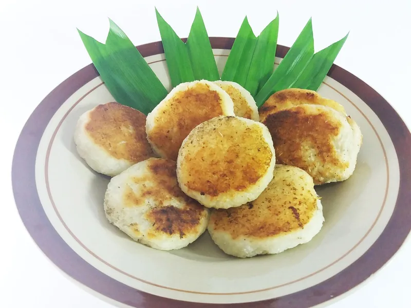 Kue wingko babat bulat berwarna kecokelatan di piring dengan hiasan daun pandan