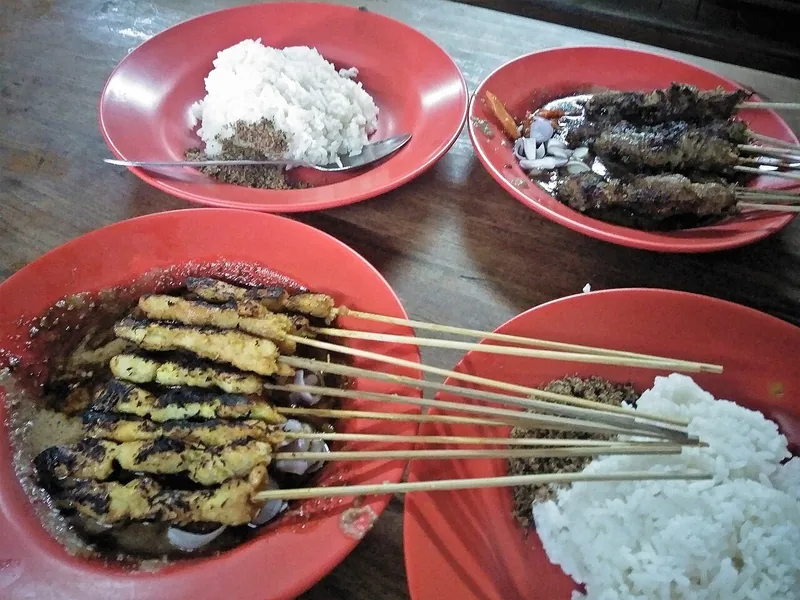 Dua macam sate bakar di piring merah bersama nasi putih bertabur serundeng