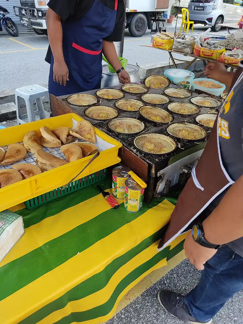 Deretan loyang besi kecil berisi adonan apam balik yang sedang dimasak di atas kompor pedagang kaki lima