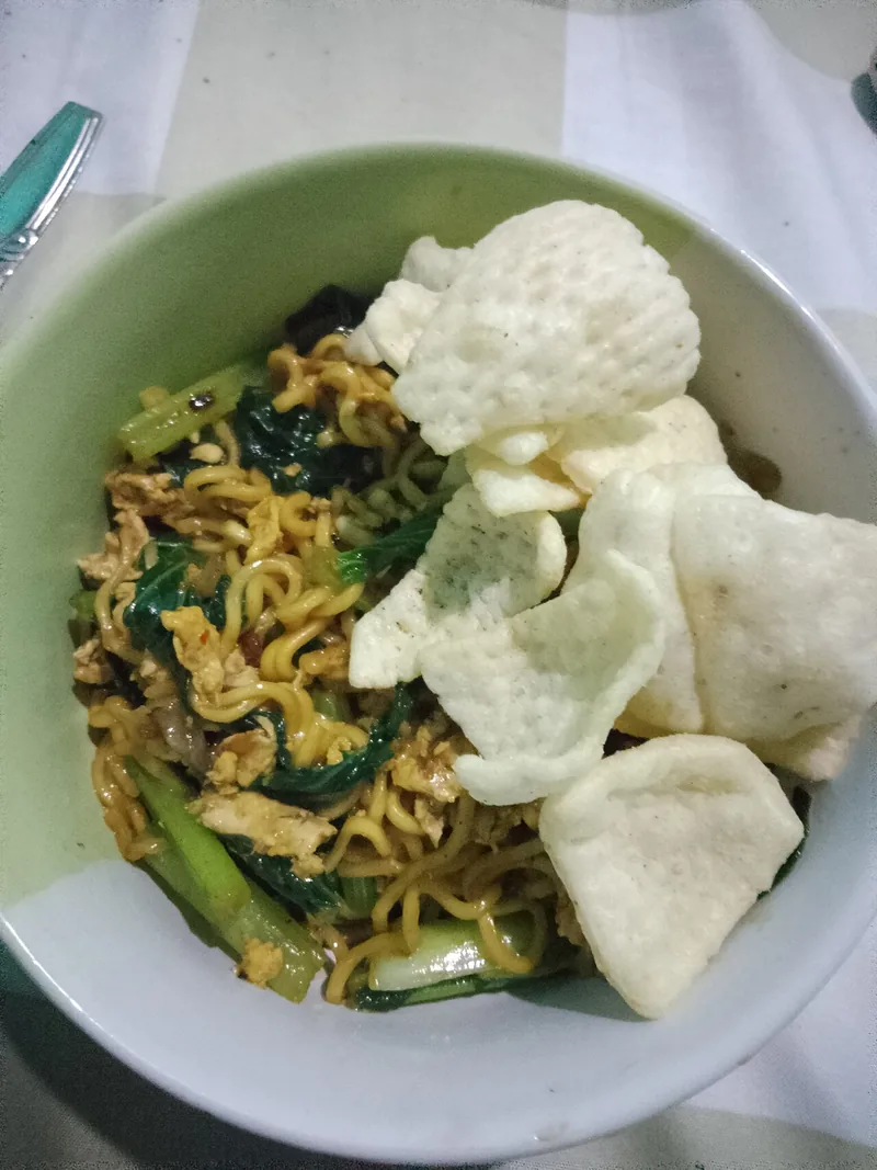 Mie nyemek dengan sawi hijau, telur orak-arik, dan kerupuk putih di mangkuk