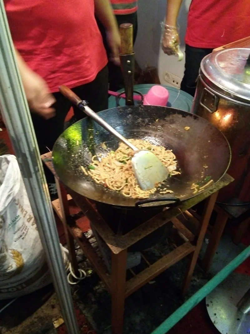 Mi kuning sedang dimasak dengan sutil di wajan hitam besar di atas kompor