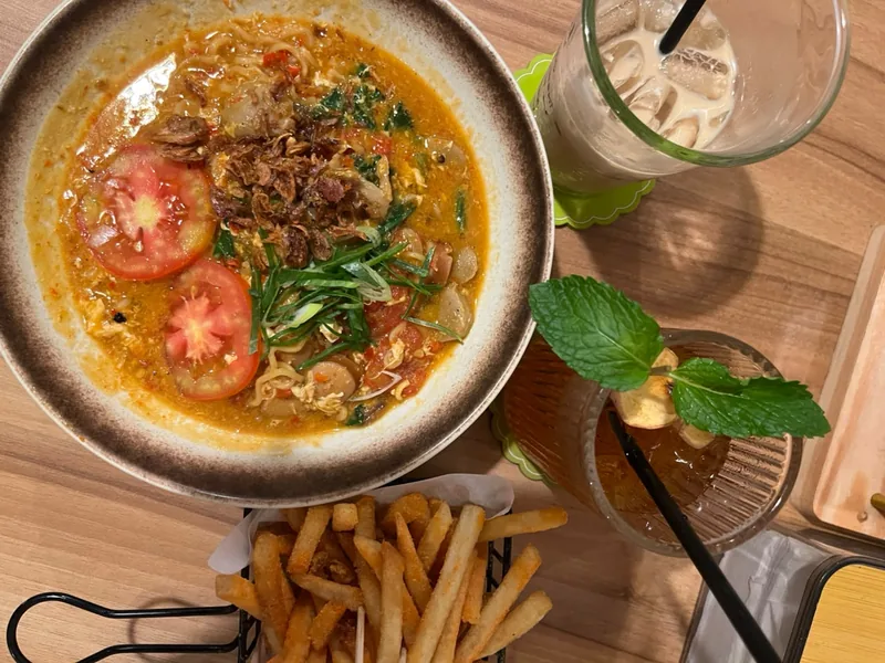 Mie nyemek kuah oranye dengan irisan tomat, bakso, daun bawang, dan bawang goreng