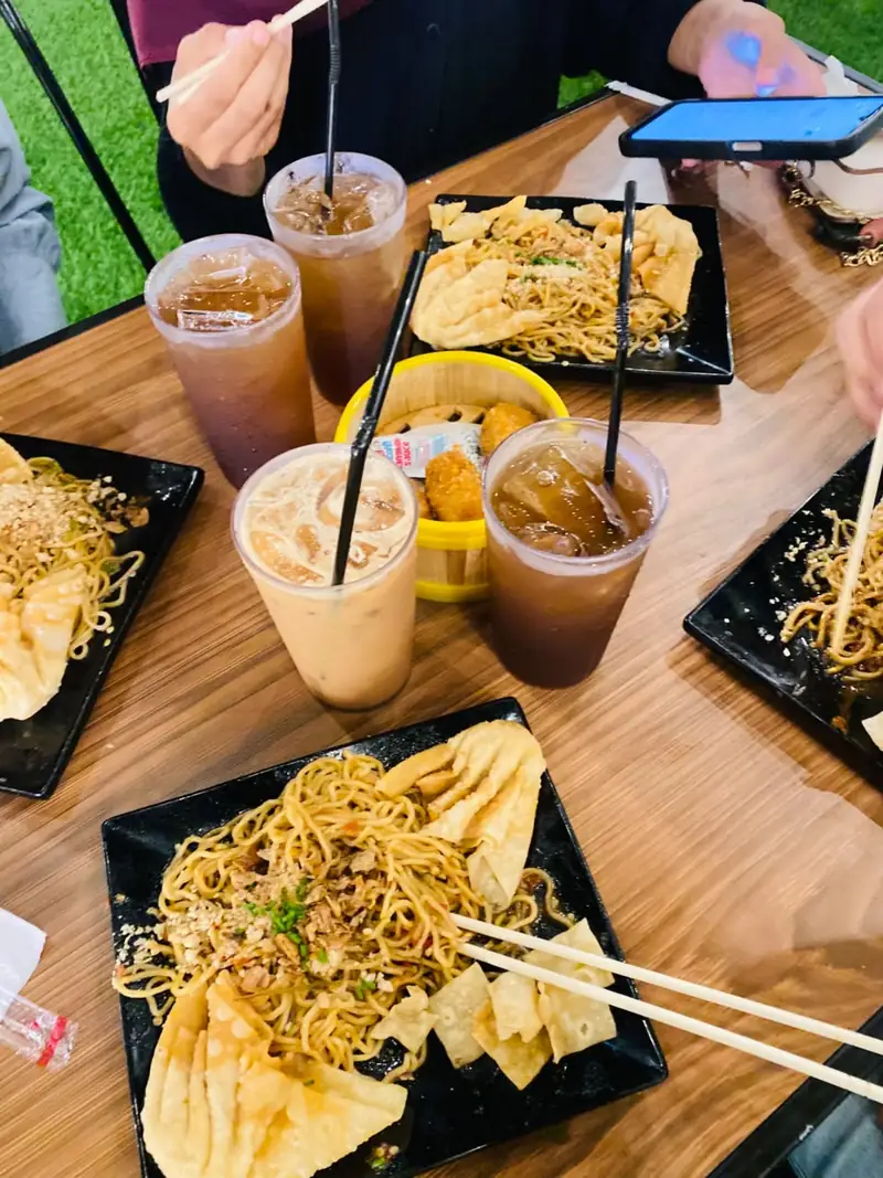 Beberapa piring mie pedas goreng dengan pangsit goreng dan es teh di meja kedai