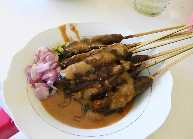 Sepiring sate daging bertusuk bambu disiram bumbu kacang dengan irisan bawang merah