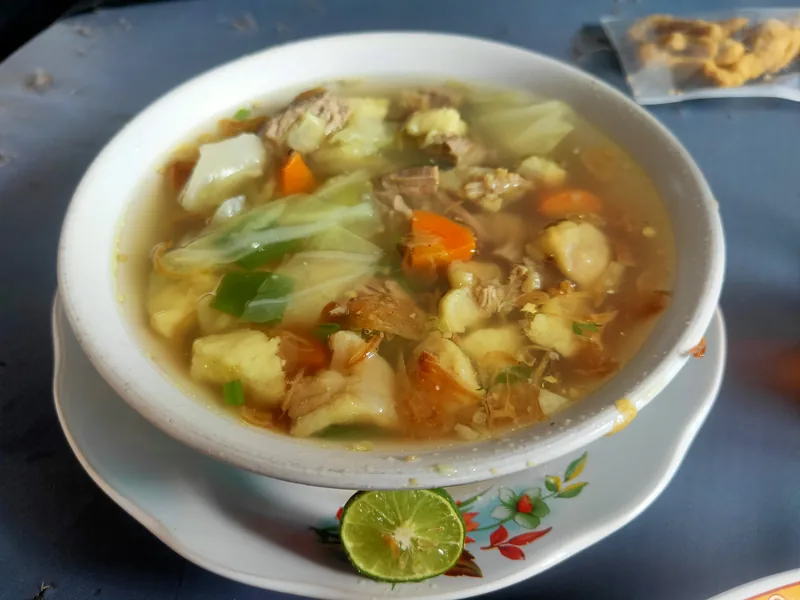 Semangkuk sop daging sapi berkuah bening dengan potongan daging, kol, wortel, dan bawang goreng