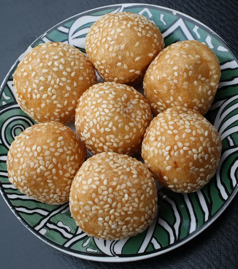 Tujuh onde-onde wijen bulat sempurna berwarna kuning keemasan tersaji di atas piring