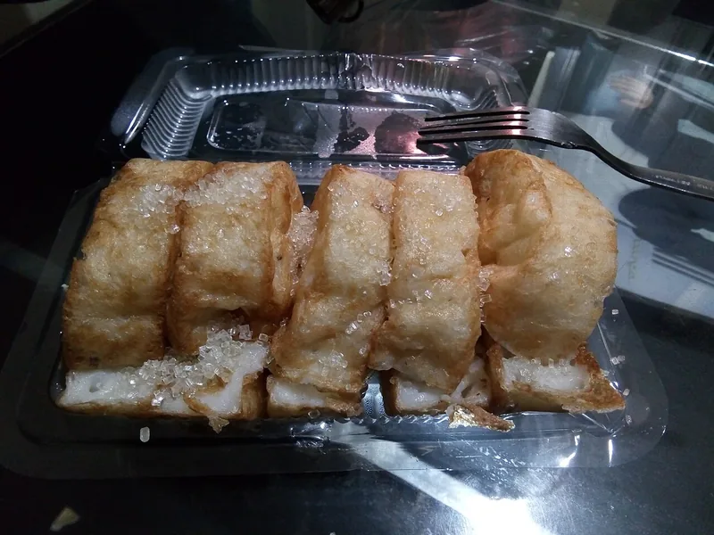 Potongan kue pancong bertabur gula pasir dalam wadah plastik bening dengan garpu