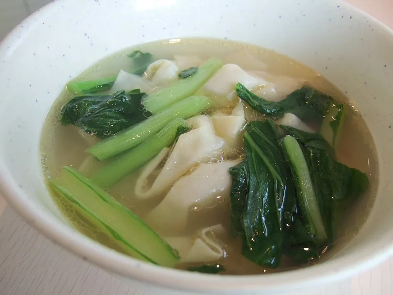 Semangkuk pangsit kuah dengan kaldu bening dan sayur sawi hijau